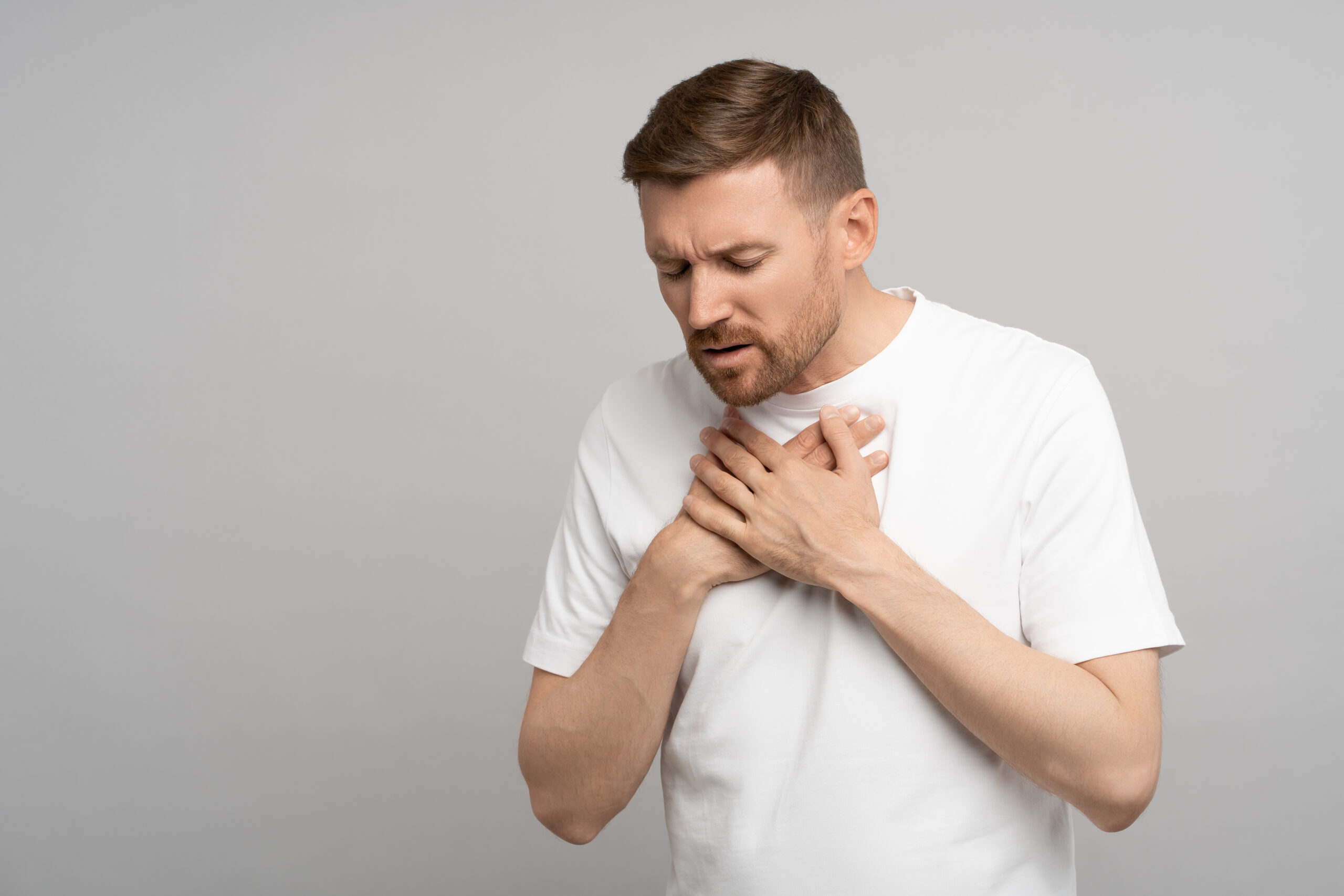 Breathing problem. Man holds on to chest suffering from heartburn. Caucasian young guy suffers from pain in sternum. Unbearable pain tearing apart chest, burning inside and suffering, acute discomfort